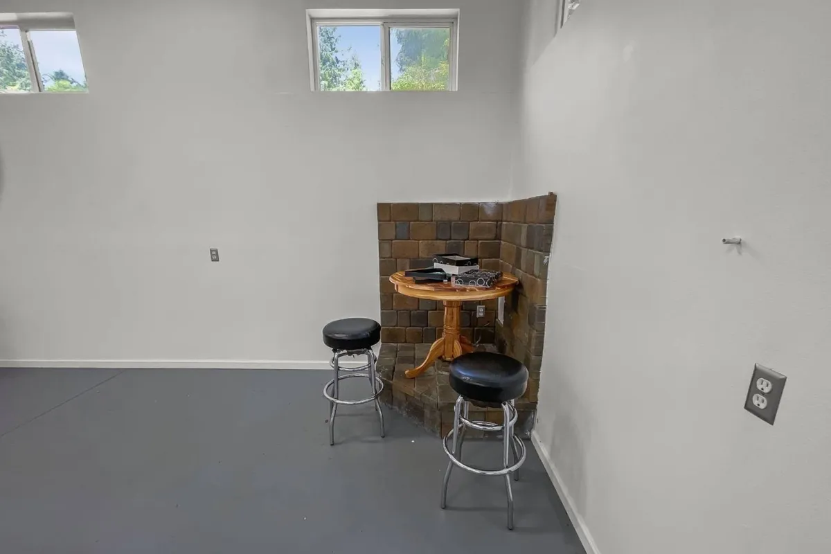 This image depicts a small, stylish kitchen scene with a round table and two bar stools set against a tiled wall. The space is set up for casual dining, conversations, and creative work. The simple yet inviting atmosphere is accentuated by thoughtful design, making it ideal for both preparing meals and gathering with others.