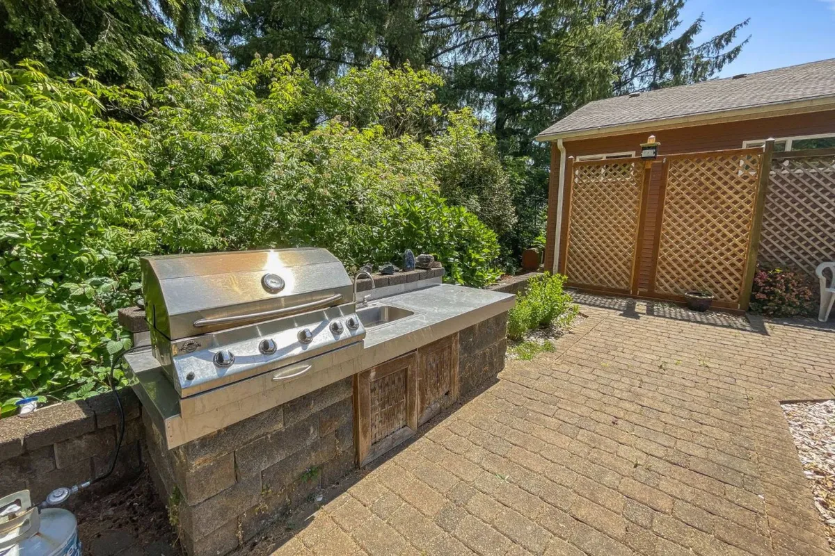 This exterior image features a grill, tidy landscaping, and a paved pathway, evoking a sense of gathering in the outdoors. The setup suggests options for group barbecues, casual dining, and shared evening moments, all within a relaxed and inviting yard space.