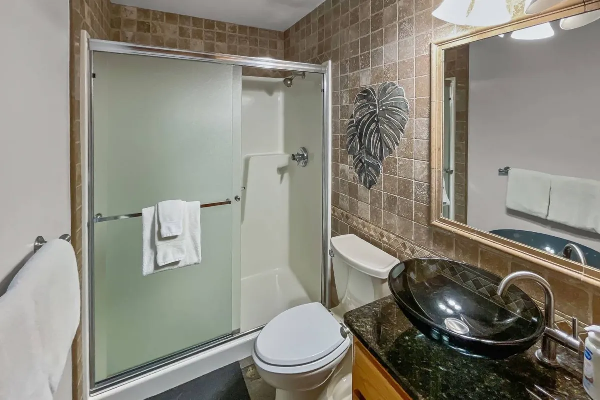A modern bathroom featuring a glass shower enclosure, sleek black granite sink, and decorative wall art. The tranquil and stylish space is designed for relaxation and convenience.
