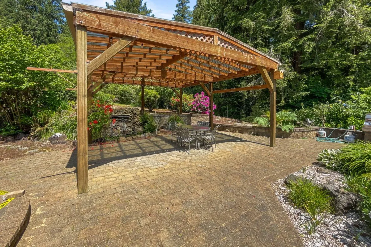 An inviting outdoor pergola with a stone seating area, surrounded by flowering plants and lush greenery. This space encourages outdoor dining, relaxation, and social gatherings amid the natural beauty of the garden.