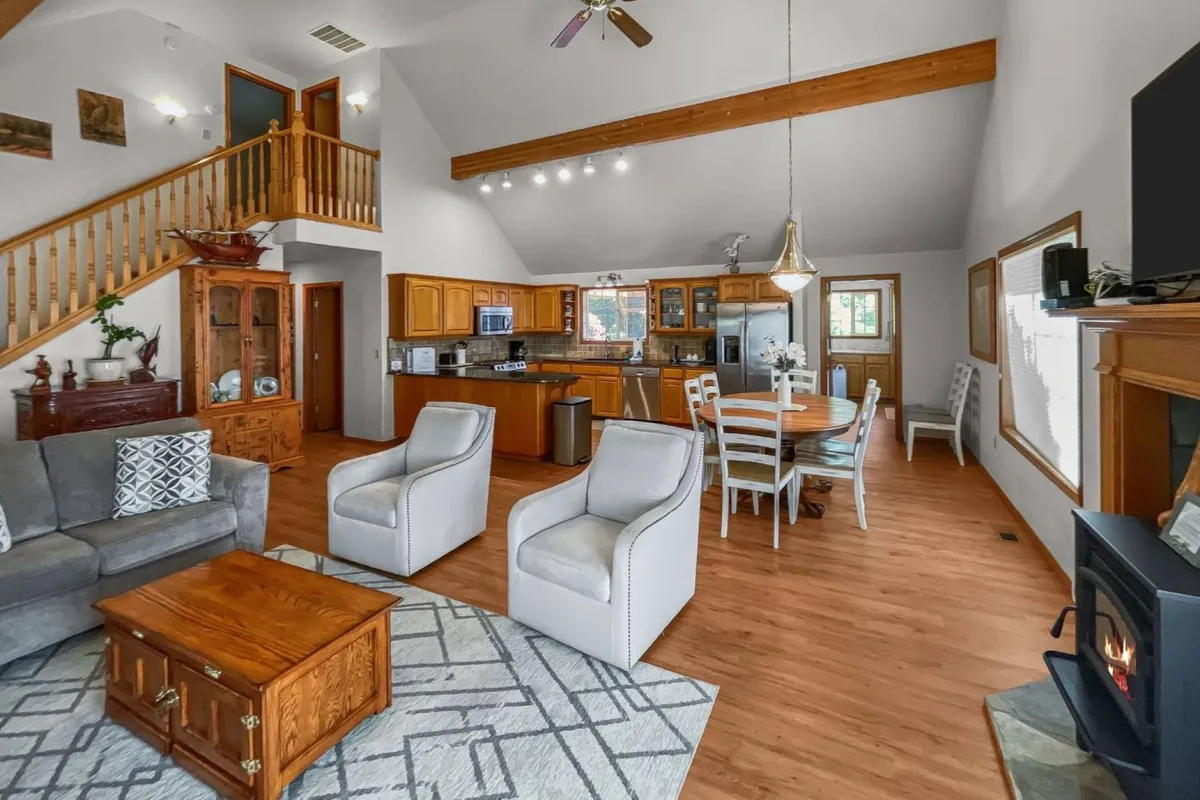 A lively family area with a sofa, dining table, kitchen island, and staircase, all set within an inviting open-plan layout. Seasonal touches and ample daylight enhance the homely vibe, emphasizing versatile gathering spaces.