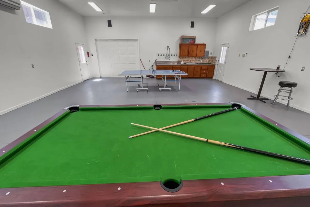 This image displays the heart of the game room, featuring both a pool table and a ping pong table, as well as a bar area in the background. The energetic vibe suggests a hub of friendly competition and social activity, with ample space for guests to gather and play.